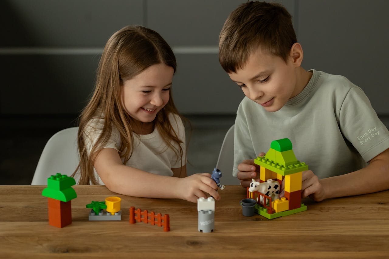 Two children play joyfully with building blocks on a wooden table indoors.